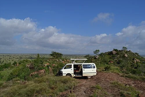 Game viewer vehicle parked on Lion Rock, in LUMO Community Wildlife Sanctuary, Kenya. The sunroof is open.