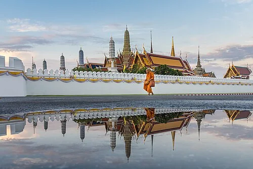 Monk walks in the morning after the rain in front of the Temple of the Emerald Buddha (Wat Phra Kaew), part of the Grand Palace, Bangkok, Thailand.